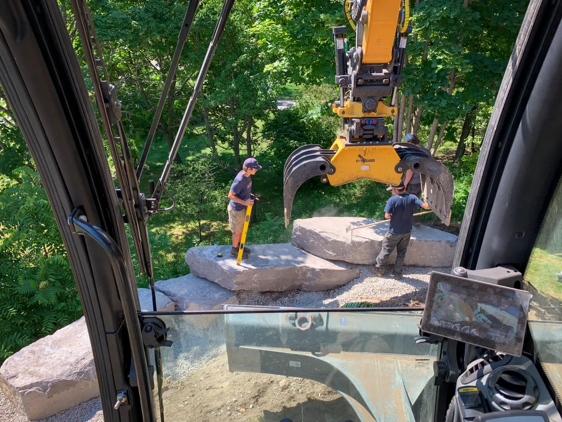Fraser's crew setting armour stone with a grapple-equipped excavator