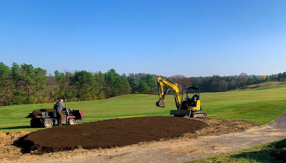 Mini excavator and utility vehicle shaping a new tee box on a golf course